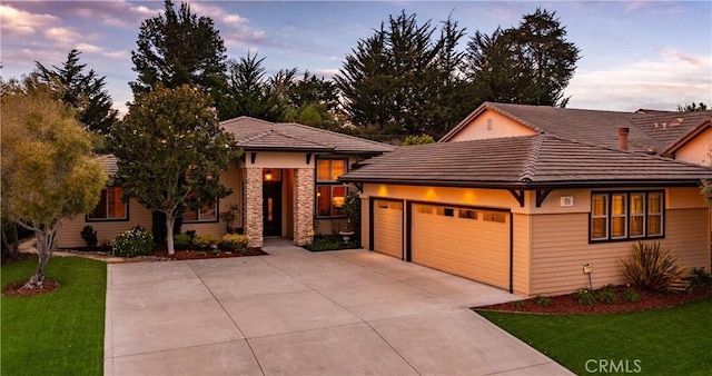 prairie-style home featuring a tiled roof, a front yard, a garage, stone siding, and driveway