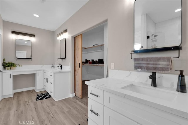 bathroom featuring a walk in closet, two vanities, a sink, and wood finished floors