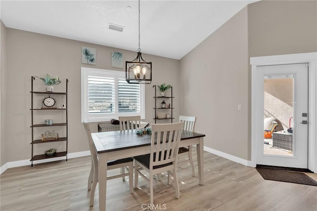 dining room with lofted ceiling, visible vents, light wood-style flooring, an inviting chandelier, and baseboards