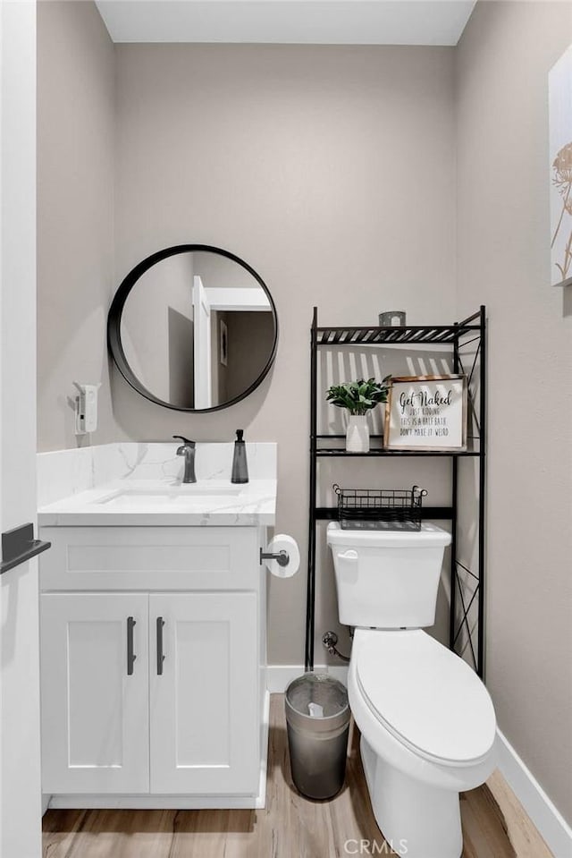 half bath with toilet, baseboards, wood finished floors, and vanity