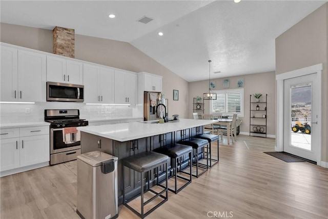 kitchen featuring visible vents, an island with sink, appliances with stainless steel finishes, white cabinetry, and backsplash