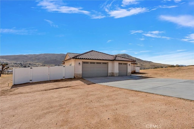 view of front of home featuring an attached garage, stone siding, concrete driveway, a gate, and stucco siding