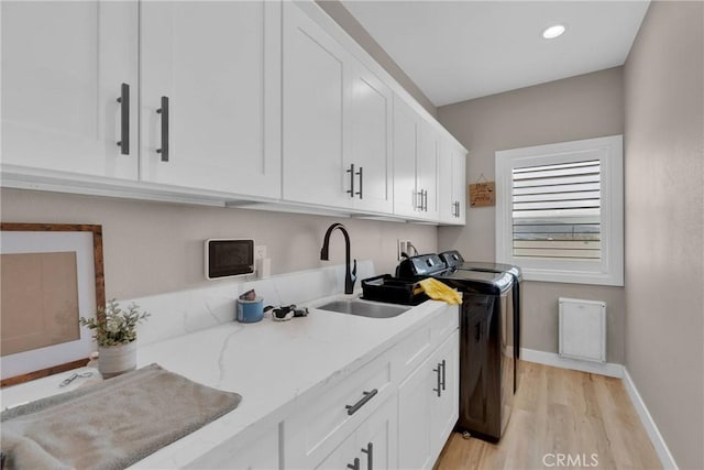 laundry area with cabinet space, baseboards, light wood-style flooring, washer and dryer, and a sink