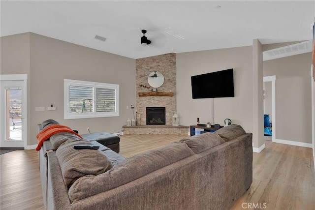 living area with light wood-type flooring, visible vents, vaulted ceiling, and a stone fireplace