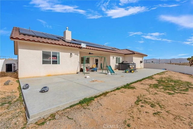 rear view of property featuring a patio, stucco siding, roof mounted solar panels, cooling unit, and a fenced backyard