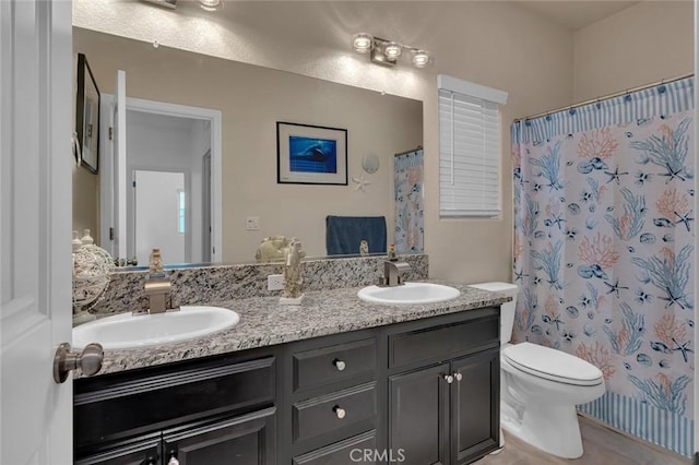 bathroom featuring toilet, double vanity, a sink, and a shower with shower curtain