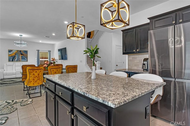 kitchen featuring a center island, decorative backsplash, freestanding refrigerator, light tile patterned flooring, and light stone countertops