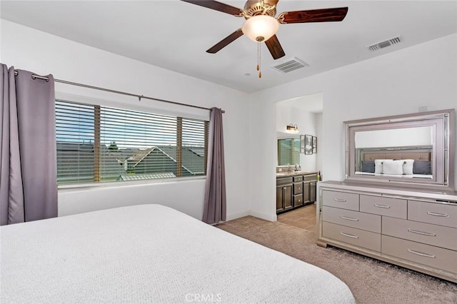 bedroom featuring a ceiling fan, light colored carpet, visible vents, and connected bathroom