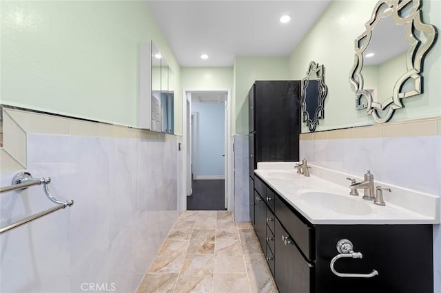 bathroom featuring recessed lighting, wainscoting, a sink, and tile walls