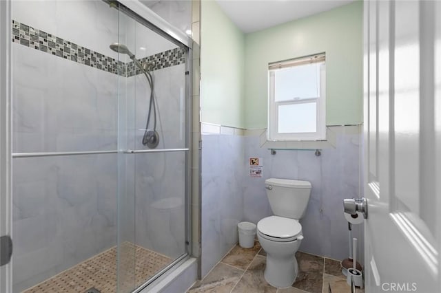 bathroom featuring toilet, a wainscoted wall, a shower stall, and tile walls