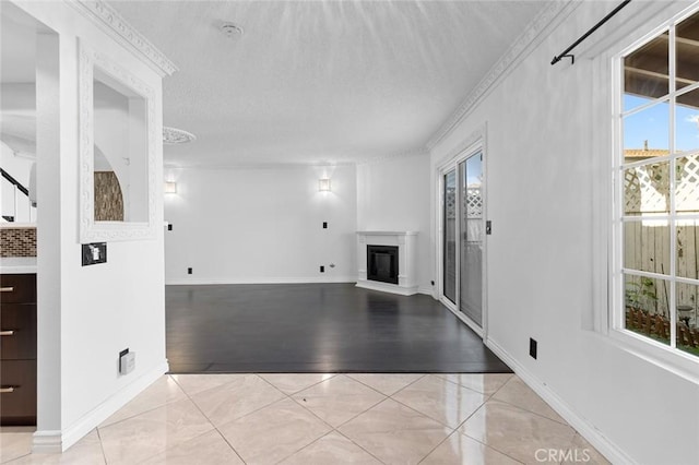 unfurnished living room featuring crown molding, light tile patterned floors, a glass covered fireplace, a textured ceiling, and baseboards