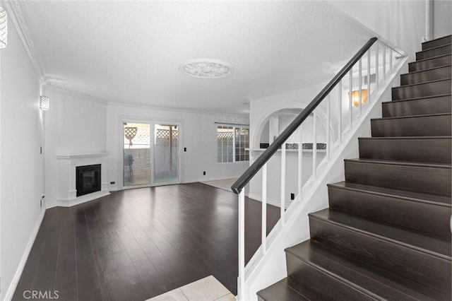 stairs with a textured ceiling, wood finished floors, baseboards, a glass covered fireplace, and crown molding