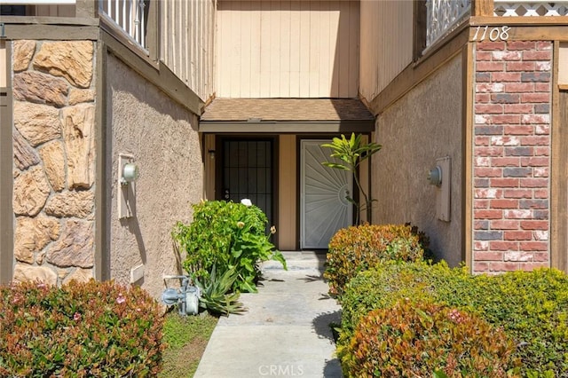 property entrance featuring brick siding, roof with shingles, and stucco siding