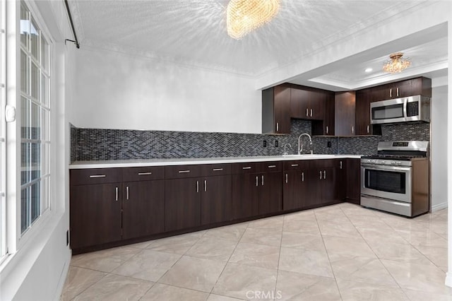 kitchen with a raised ceiling, appliances with stainless steel finishes, ornamental molding, light countertops, and a sink