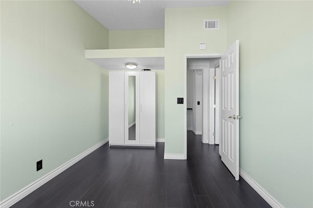 spare room with dark wood-style floors, visible vents, and baseboards