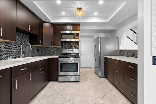 kitchen featuring a raised ceiling, appliances with stainless steel finishes, a sink, and light countertops