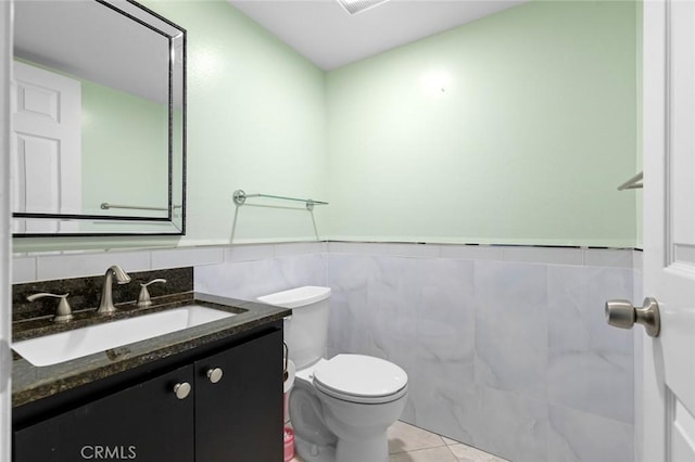 half bathroom with toilet, a wainscoted wall, tile patterned floors, vanity, and tile walls