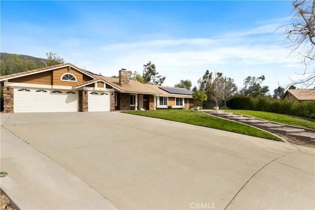 view of front of home featuring stone siding, roof mounted solar panels, a front lawn, and a garage