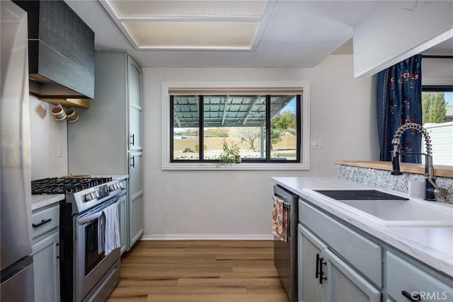 kitchen with stainless steel appliances, light countertops, a sink, light wood-type flooring, and baseboards