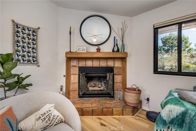 living area featuring a healthy amount of sunlight, a fireplace, baseboards, and wood finished floors