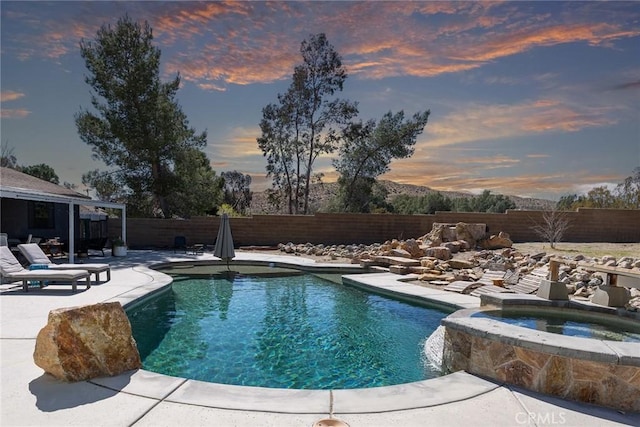 pool at dusk featuring an in ground hot tub, a fenced backyard, a fenced in pool, and a patio