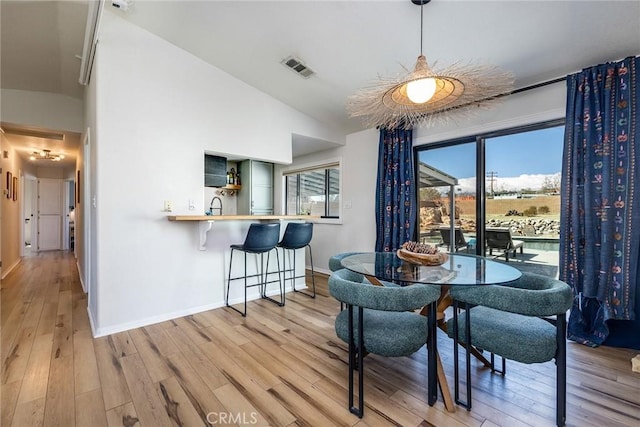 dining space with visible vents, vaulted ceiling, light wood-style flooring, and baseboards