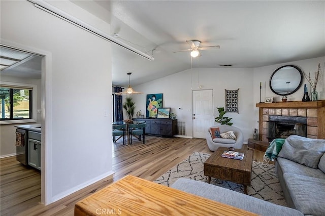 living area featuring lofted ceiling, light wood finished floors, a tile fireplace, and visible vents