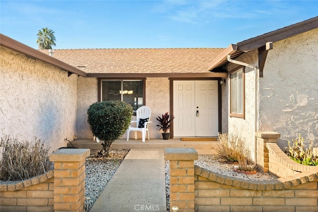 view of exterior entry featuring a shingled roof and stucco siding