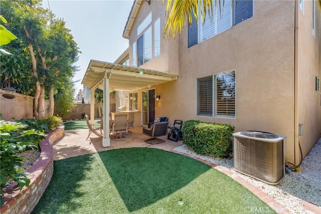 rear view of house with a lawn, fence private yard, central air condition unit, a patio area, and stucco siding