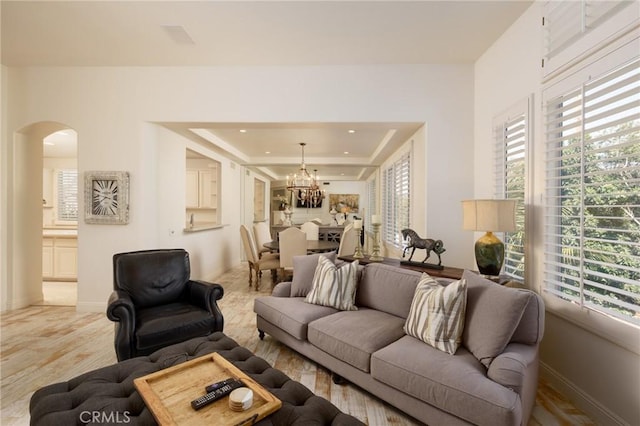 living area with baseboards, arched walkways, a chandelier, and a raised ceiling