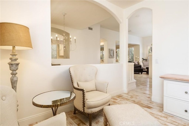 living area with arched walkways, a notable chandelier, visible vents, light wood-type flooring, and baseboards