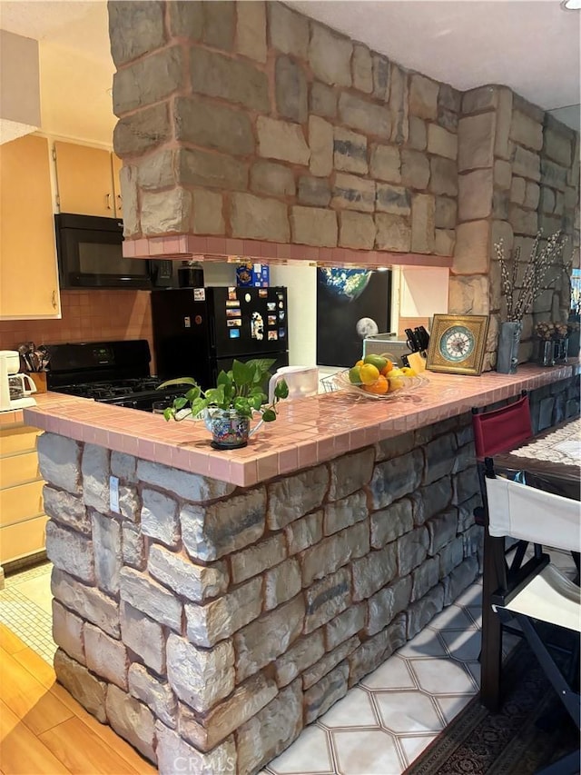 interior space featuring tile countertops, black appliances, and a peninsula