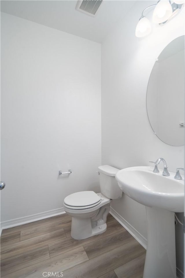 bathroom with toilet, wood finished floors, visible vents, and baseboards