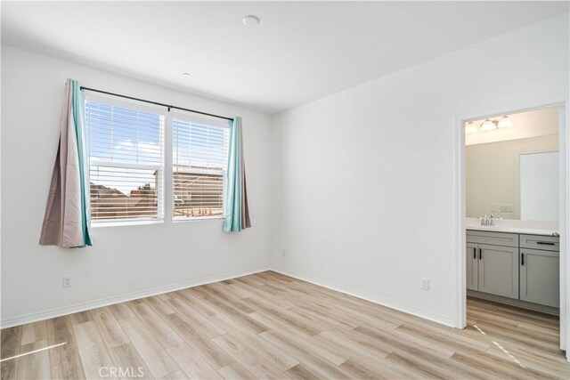 spare room with a sink, light wood-style flooring, and baseboards