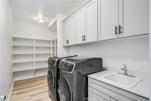 clothes washing area featuring cabinet space, baseboards, washer and clothes dryer, light wood-style flooring, and a sink