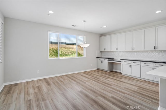 kitchen with light wood-style floors, white cabinets, built in study area, and backsplash