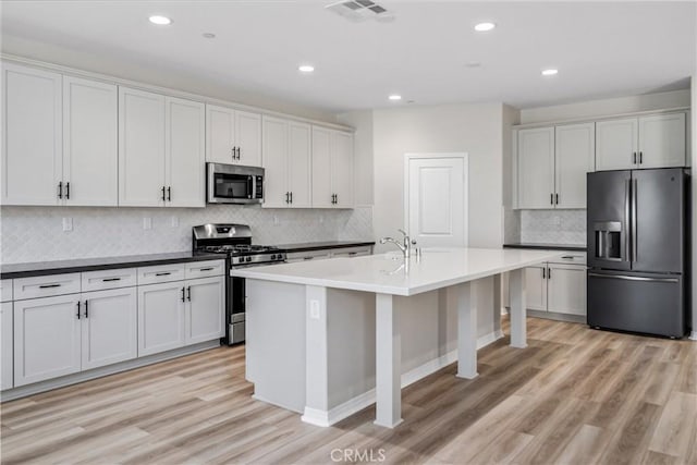 kitchen featuring a kitchen island with sink, recessed lighting, stainless steel appliances, visible vents, and light wood-style floors