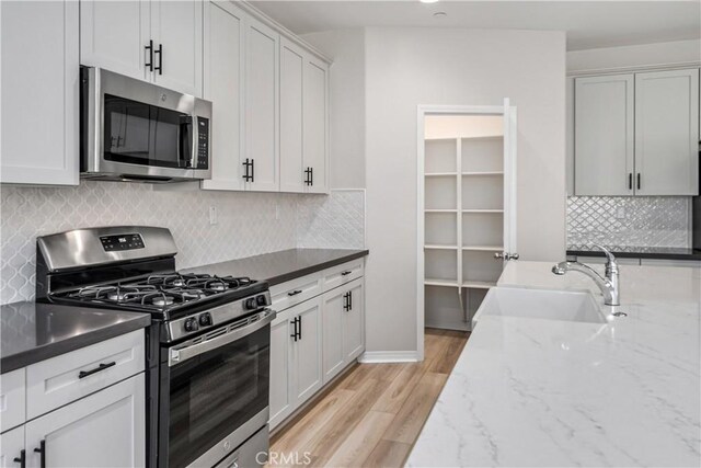 kitchen with appliances with stainless steel finishes, light stone counters, a sink, light wood-style floors, and backsplash