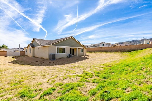 rear view of property featuring central AC unit, fence, and stucco siding