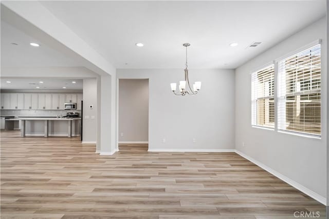 unfurnished dining area with visible vents, light wood-style flooring, baseboards, and an inviting chandelier