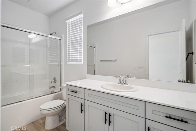 bathroom with enclosed tub / shower combo, vanity, toilet, and wood finished floors