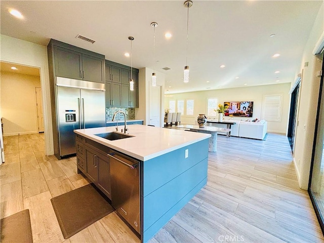 kitchen featuring a kitchen island with sink, stainless steel appliances, light countertops, light wood-type flooring, and a sink