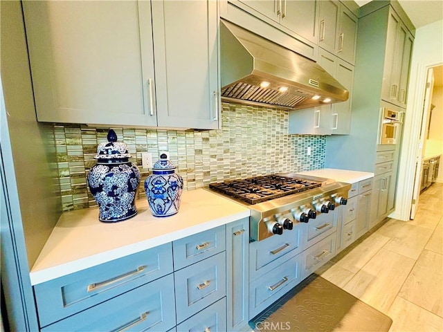 kitchen with tasteful backsplash, light countertops, stainless steel gas stovetop, and under cabinet range hood