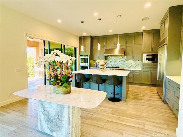 kitchen featuring stainless steel appliances, light countertops, ventilation hood, tasteful backsplash, and a kitchen bar