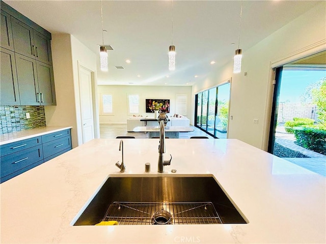 kitchen with tasteful backsplash, light countertops, a sink, and hanging light fixtures