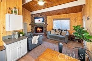 living room featuring wooden walls, lofted ceiling with beams, wooden ceiling, ceiling fan, and a stone fireplace