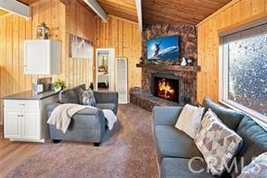 living room featuring lofted ceiling with beams, wood walls, wood ceiling, and a stone fireplace