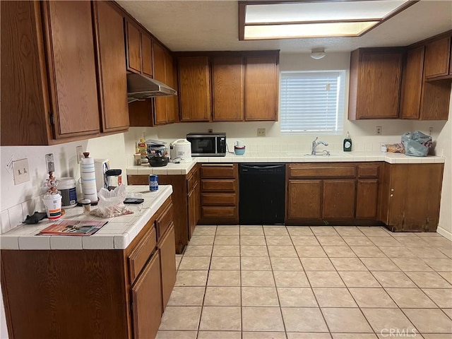 kitchen with under cabinet range hood, a sink, black dishwasher, tile counters, and stainless steel microwave