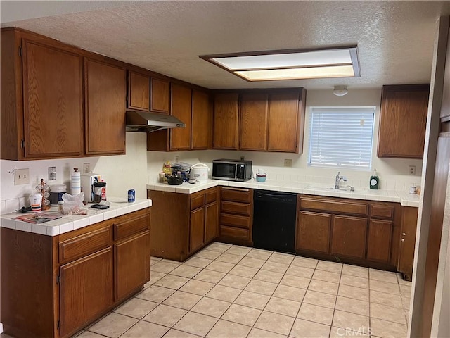 kitchen featuring under cabinet range hood, black dishwasher, stainless steel microwave, and tile counters