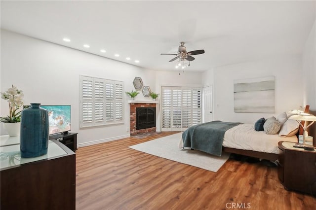 bedroom featuring baseboards, ceiling fan, wood finished floors, a brick fireplace, and recessed lighting